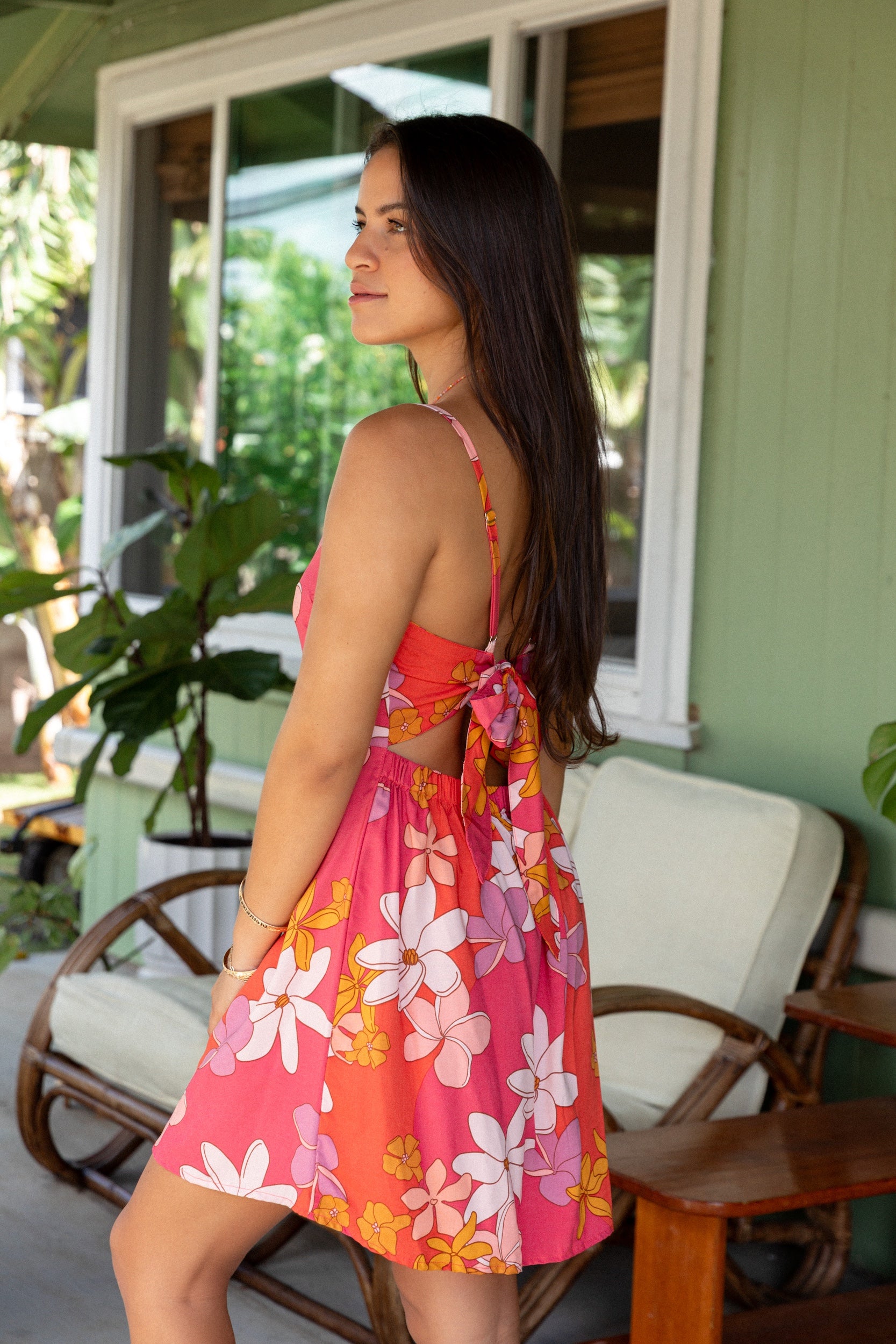 woman with brown hair wearing a pink mini spaghetti strap dress with retro flower print and tie back detail 