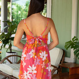 woman with brown hair wearing a pink mini spaghetti strap dress with retro flower print and tie back detail 