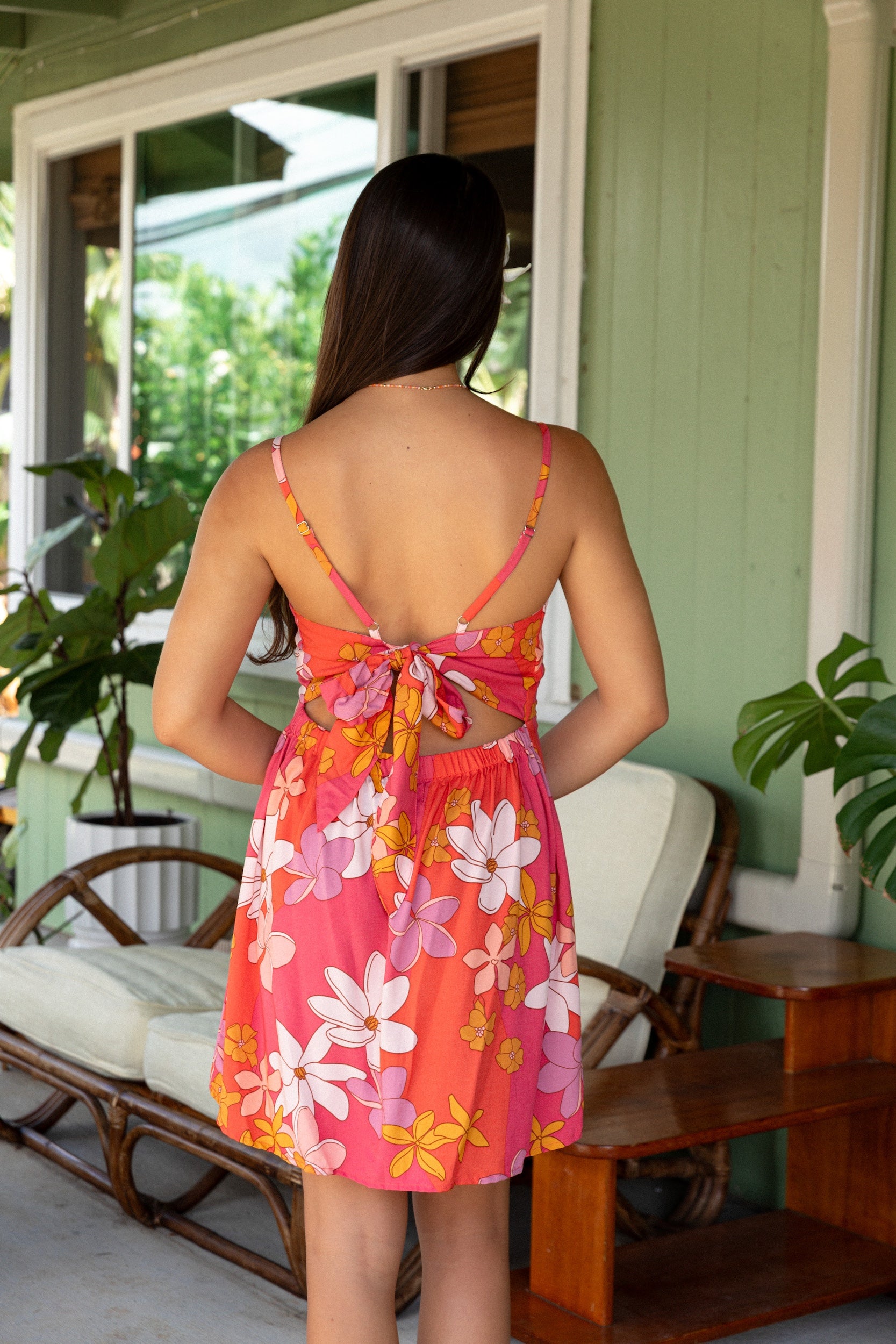 woman with brown hair wearing a pink mini spaghetti strap dress with retro flower print and tie back detail 