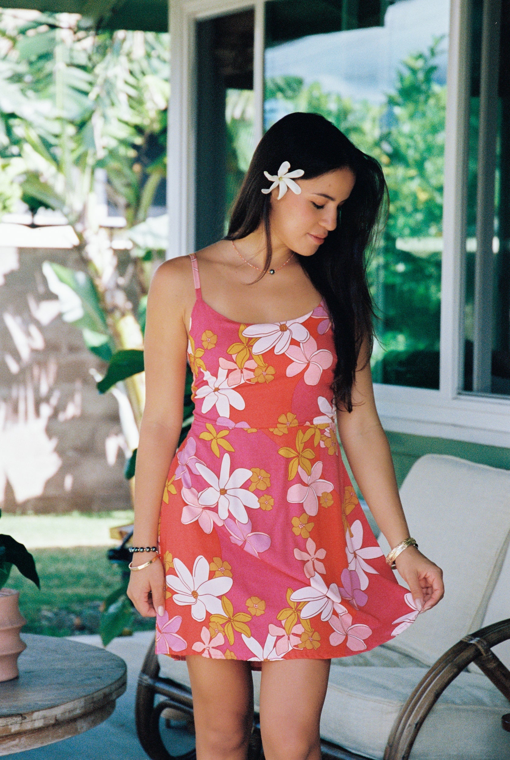 woman with brown hair wearing a pink mini spaghetti strap dress with retro flower print and tie back detail 