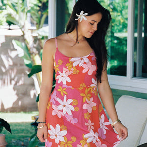 woman with brown hair wearing a pink mini spaghetti strap dress with retro flower print and tie back detail 