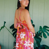 woman with brown hair wearing a pink mini spaghetti strap dress with retro flower print and tie back detail 