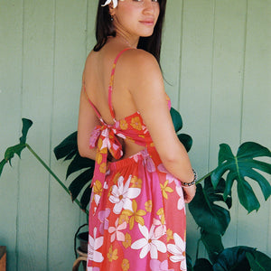 woman with brown hair wearing a pink mini spaghetti strap dress with retro flower print and tie back detail 