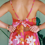 woman with brown hair wearing a pink mini spaghetti strap dress with retro flower print and tie back detail 