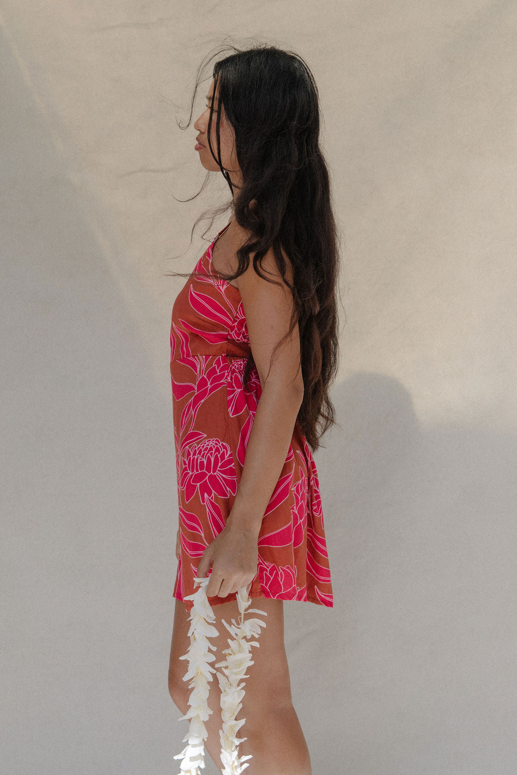 woman with brown hair wearing a sienna colored mini dress with tie back detail and awapuhi pattern