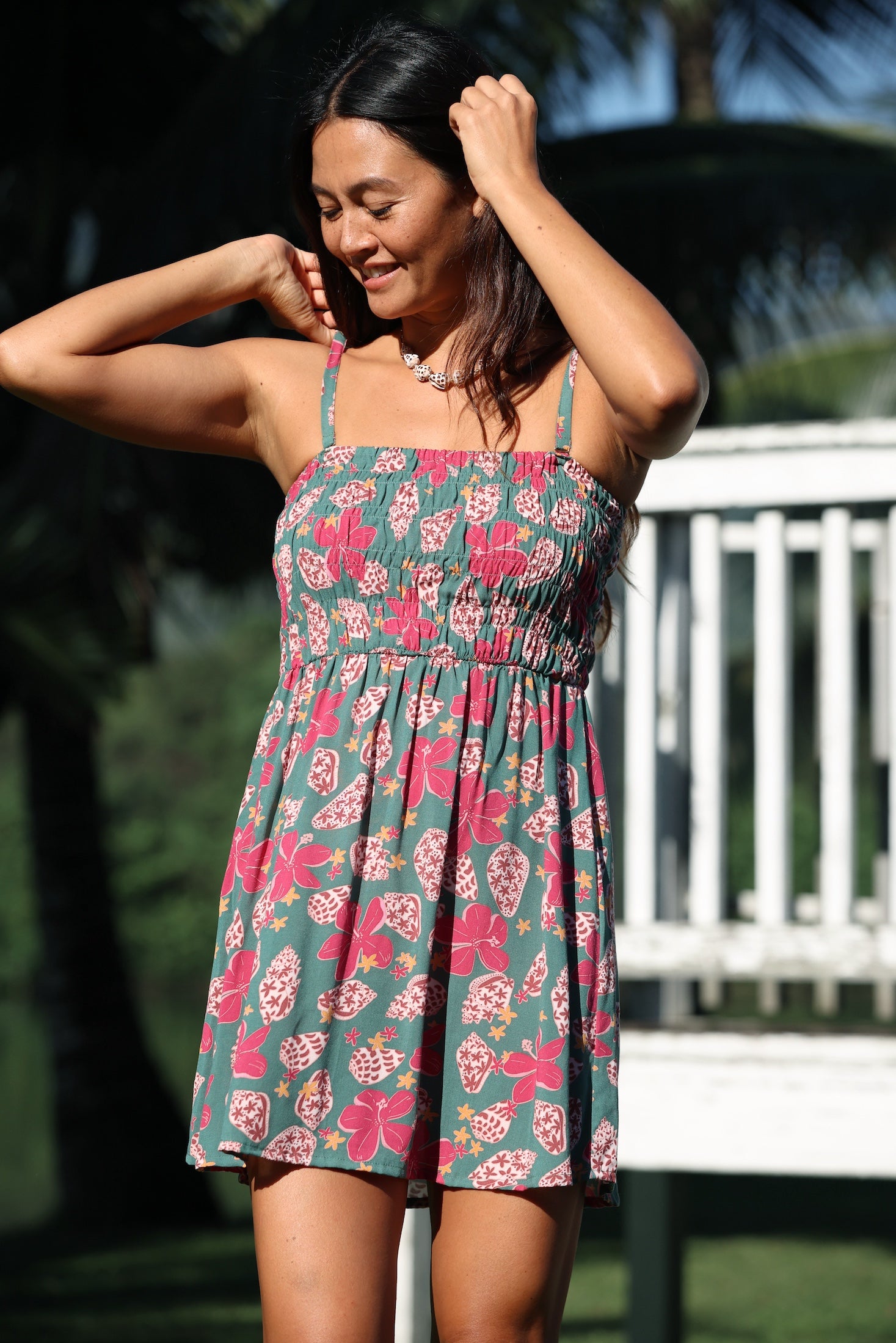 woman with brown hair wearing a teal mini dress with removable straps and smocked bodice with shell and pua print