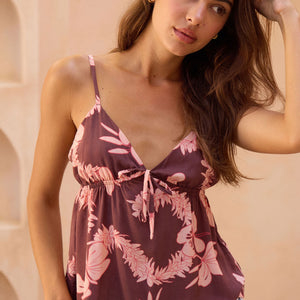 woman with brown hair wearing brown/maroon toned spaghetti strap top with bow detail and pink lei awapuhi print