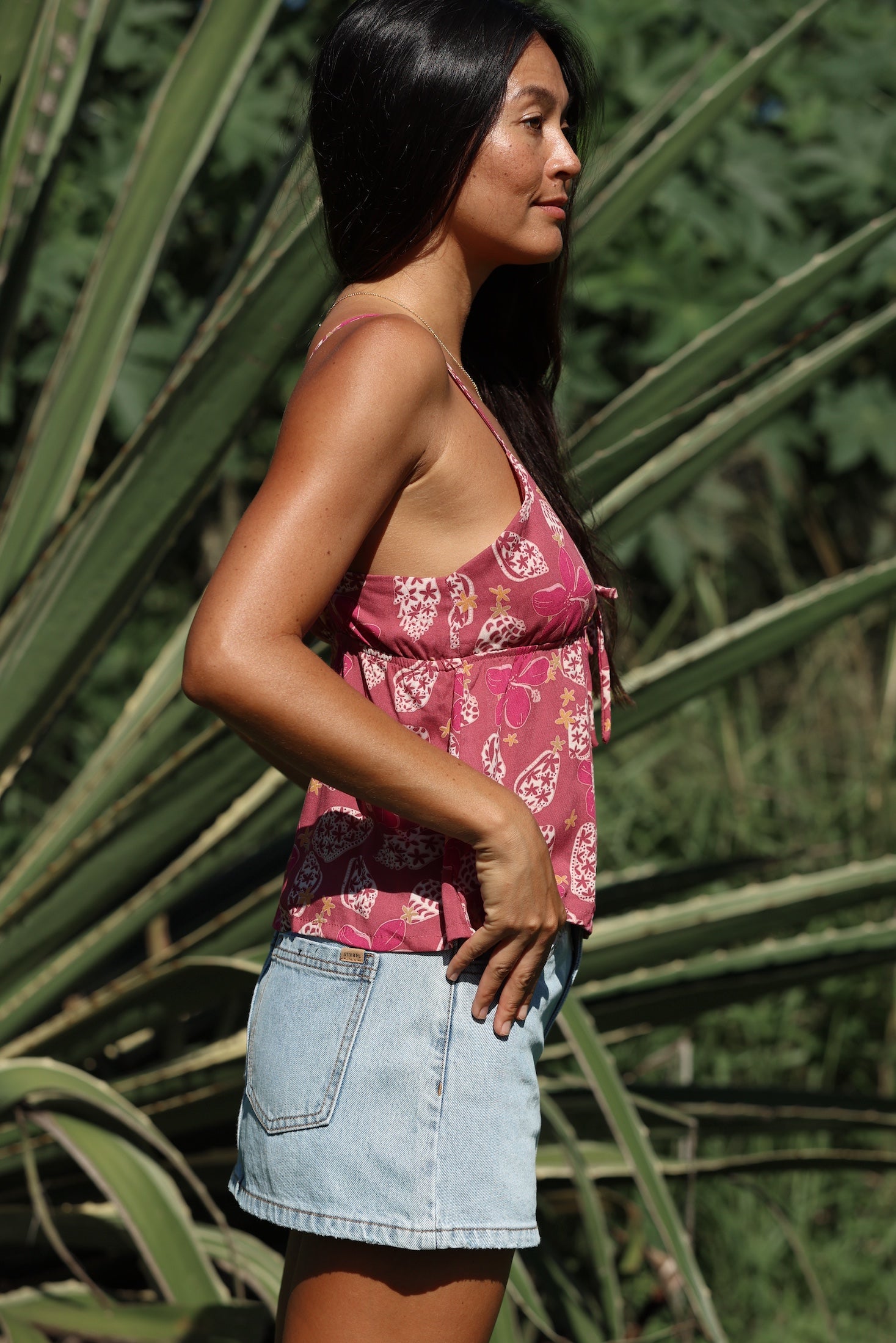 woman with brown hair wearing a pink spaghetti strap top with bow detail with shell and pua print