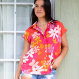 women with brown hair wearing a pink short sleeve button up top with retro flower pattern