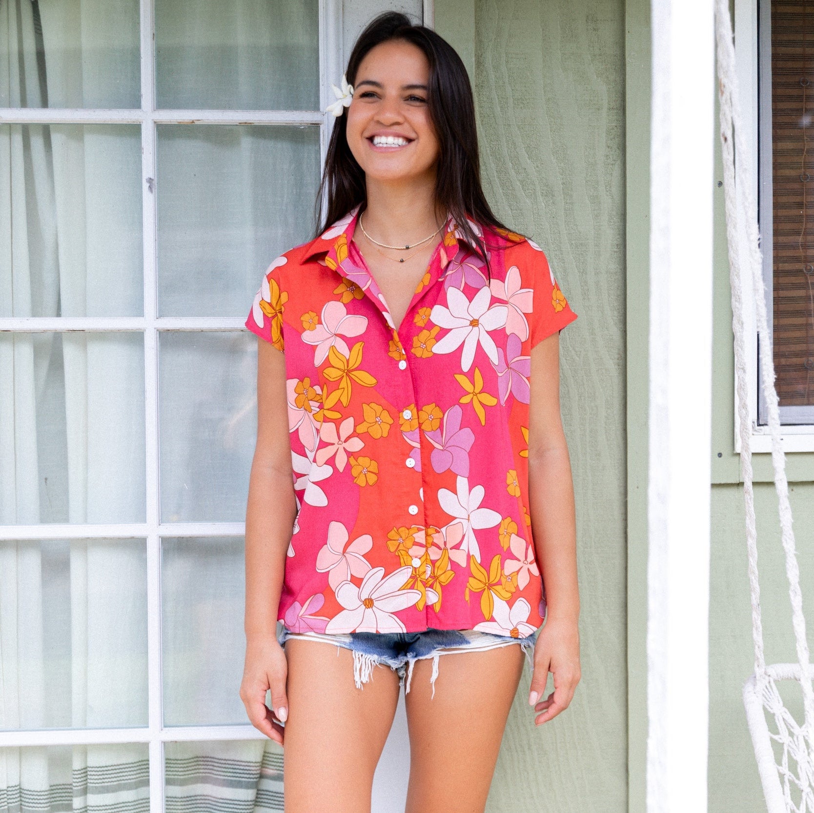 women with brown hair wearing a pink short sleeve button up top with retro flower pattern