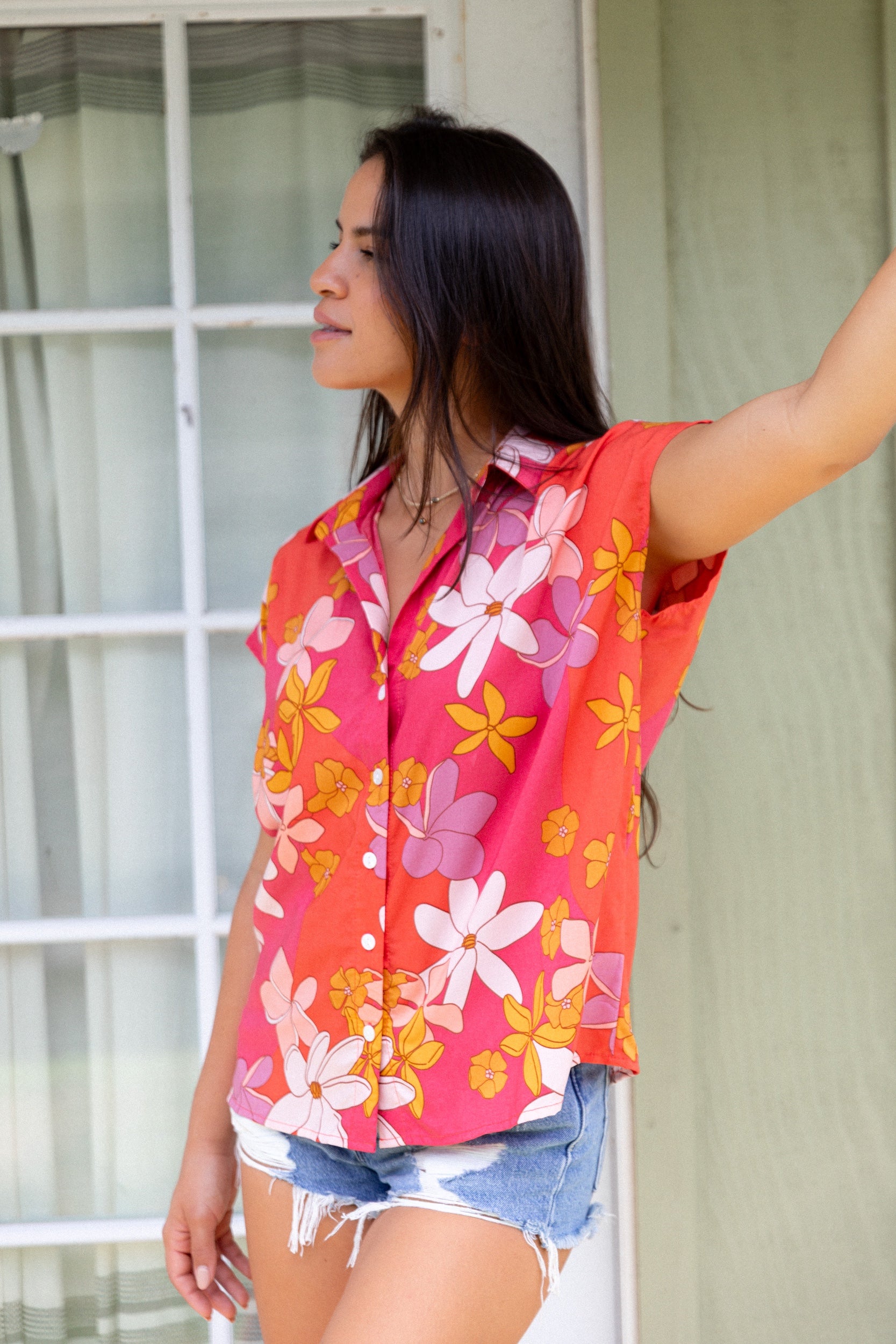 women with brown hair wearing a pink short sleeve button up top with retro flower pattern