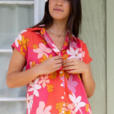 women with brown hair wearing a pink short sleeve button up top with retro flower pattern