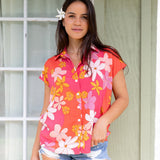 women with brown hair wearing a pink short sleeve button up top with retro flower pattern