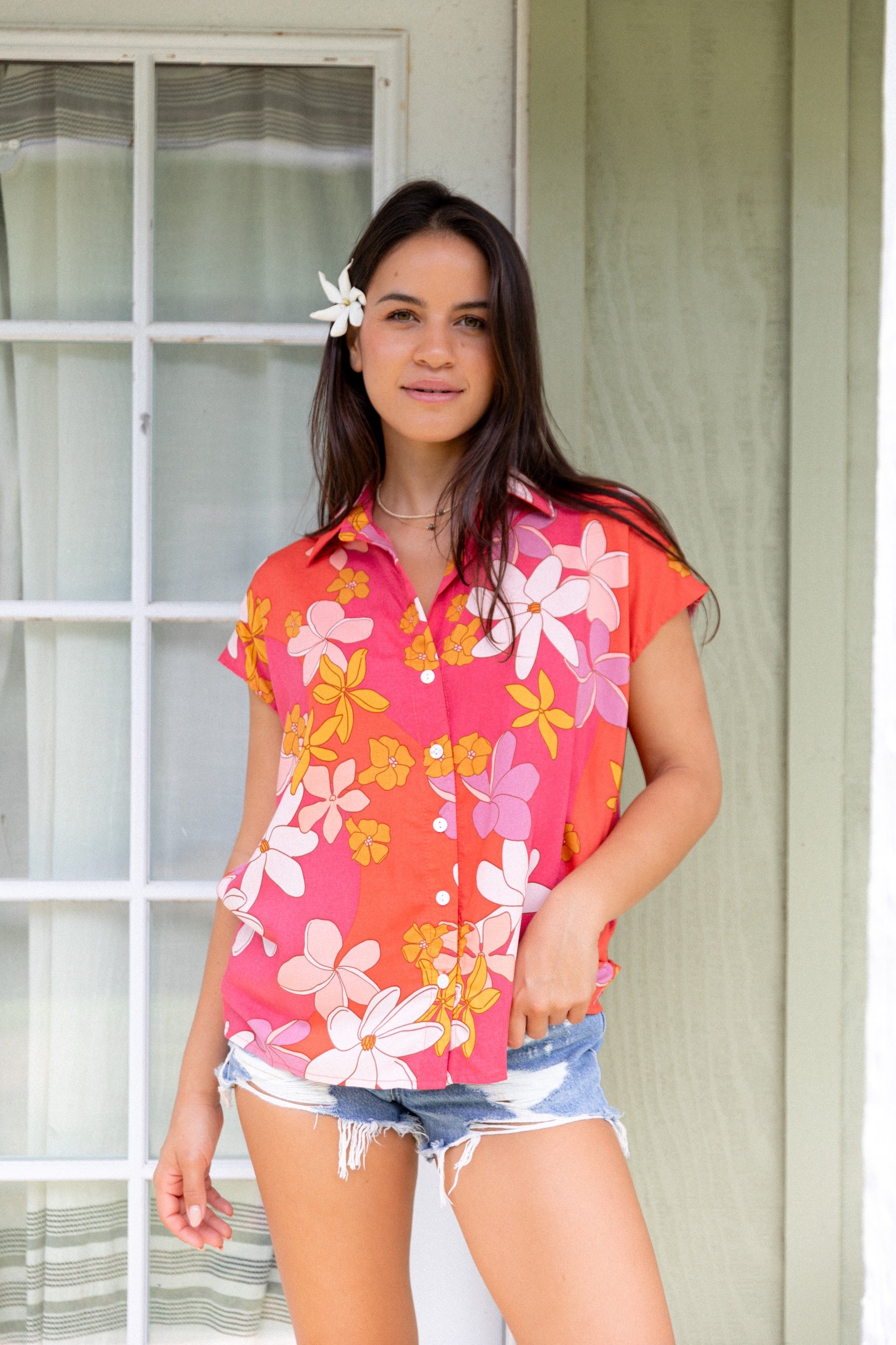 women with brown hair wearing a pink short sleeve button up top with retro flower pattern
