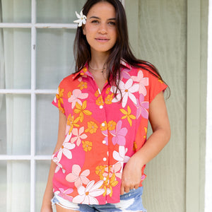 women with brown hair wearing a pink short sleeve button up top with retro flower pattern
