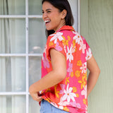 women with brown hair wearing a pink short sleeve button up top with retro flower pattern