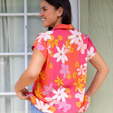 women with brown hair wearing a pink short sleeve button up top with retro flower pattern