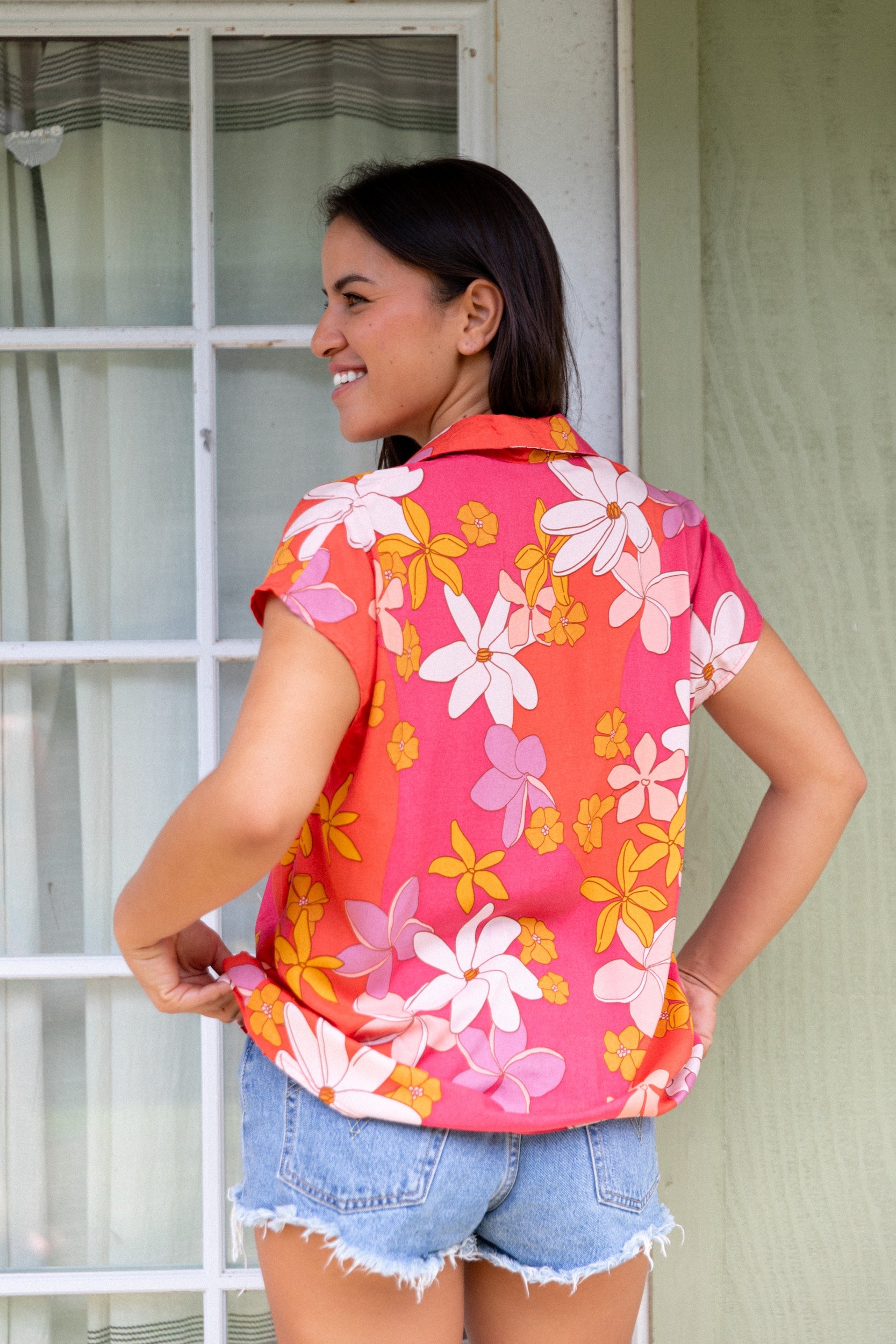 women with brown hair wearing a pink short sleeve button up top with retro flower pattern