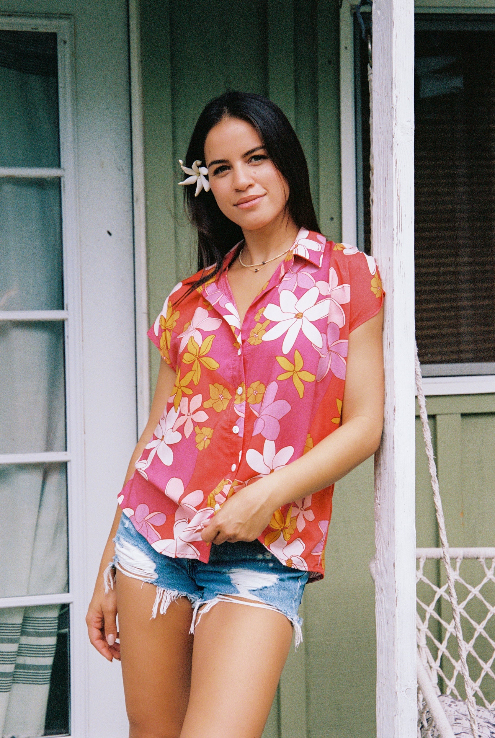 women with brown hair wearing a pink short sleeve button up top with retro flower pattern