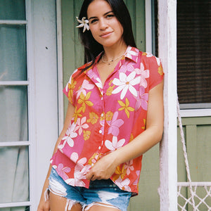 women with brown hair wearing a pink short sleeve button up top with retro flower pattern