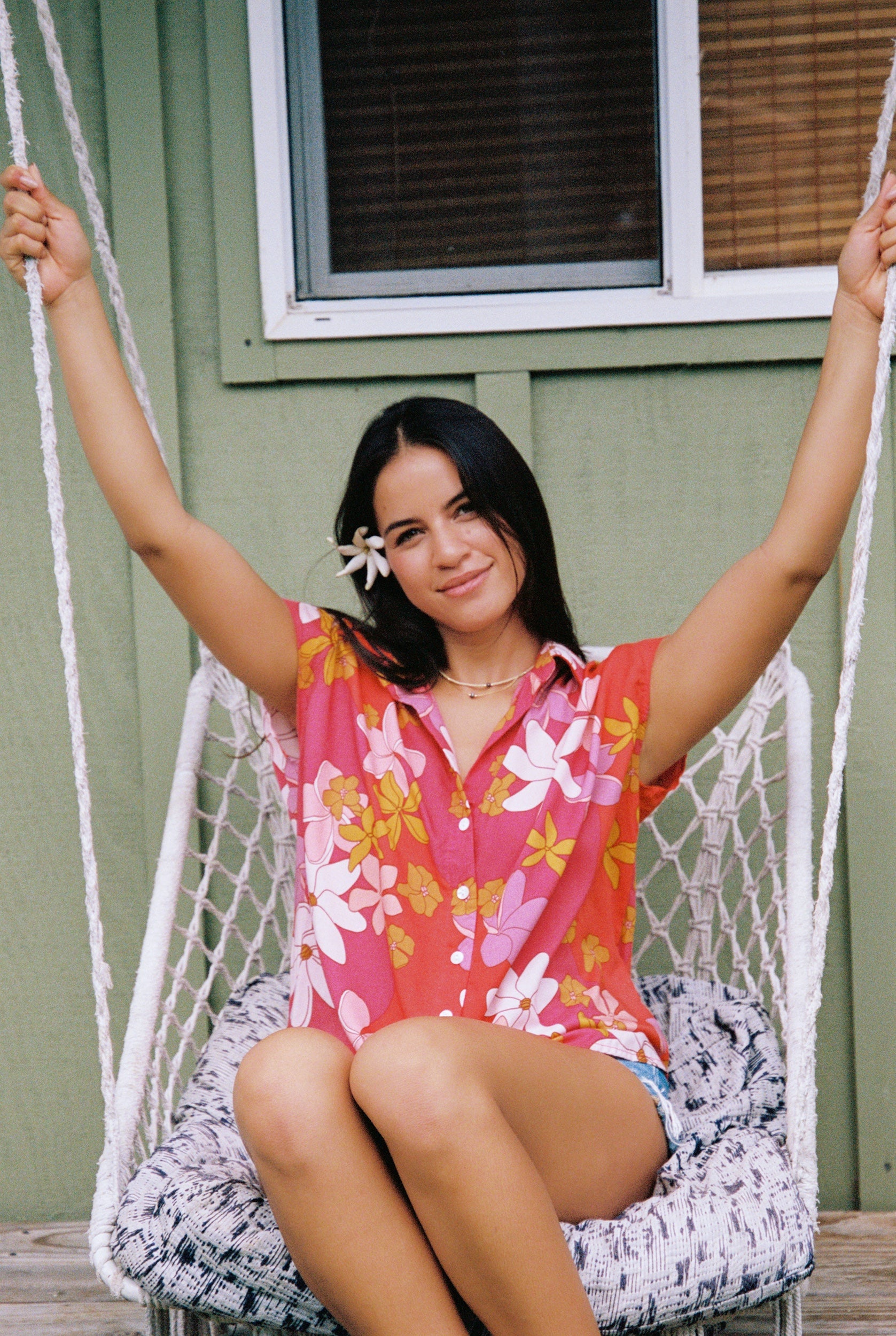 women with brown hair wearing a pink short sleeve button up top with retro flower pattern
