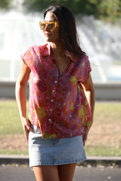 woman wearing terracotta colored button up top with large purple and yellow flower pattern