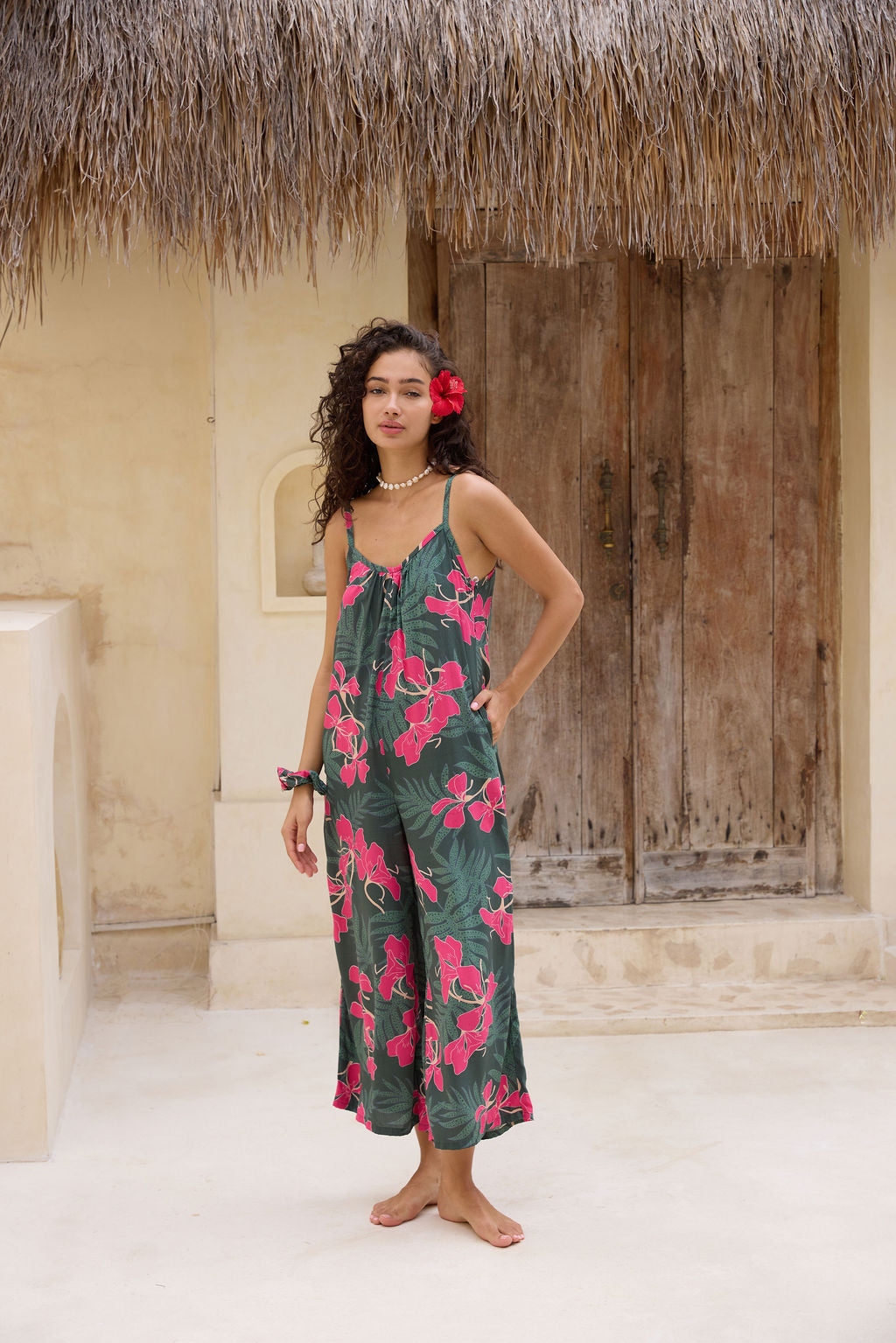 woman with brown hair wearing a dark green spaghetti strap jumpsuit with fern and ginger print