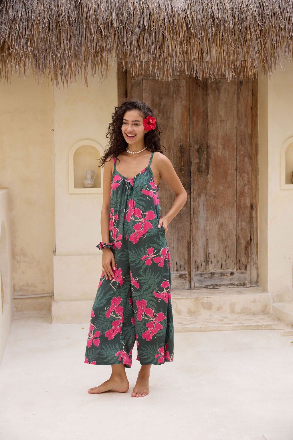 woman with brown hair wearing a dark green spaghetti strap jumpsuit with fern and ginger print