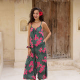 woman with brown hair wearing a dark green spaghetti strap jumpsuit with fern and ginger print