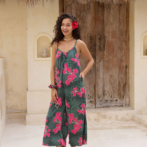 woman with brown hair wearing a dark green spaghetti strap jumpsuit with fern and ginger print