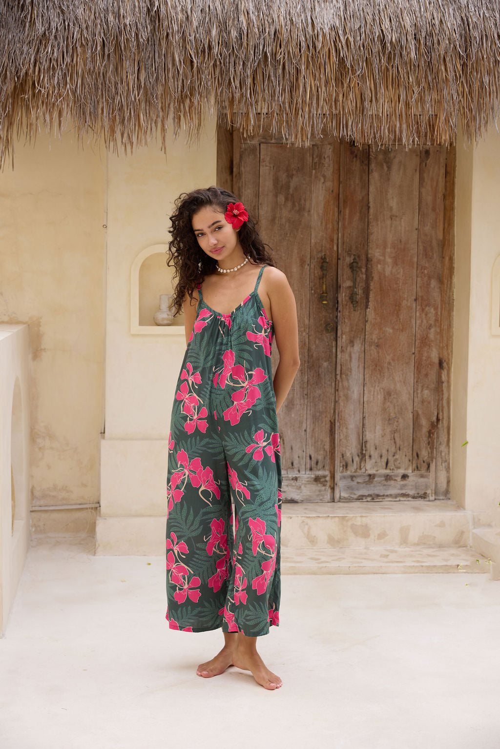 woman with brown hair wearing a dark green spaghetti strap jumpsuit with fern and ginger print