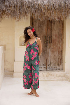 woman with brown hair wearing a dark green spaghetti strap jumpsuit with fern and ginger print