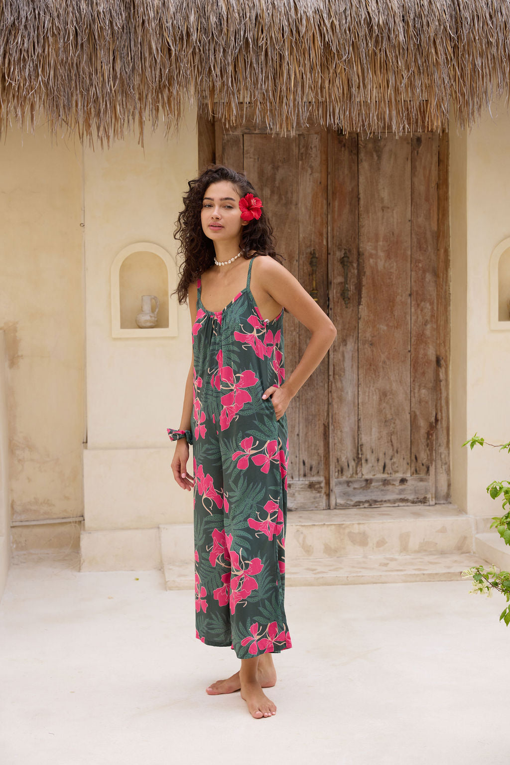 woman with brown hair wearing a dark green spaghetti strap jumpsuit with fern and ginger print