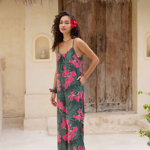 woman with brown hair wearing a dark green spaghetti strap jumpsuit with fern and ginger print