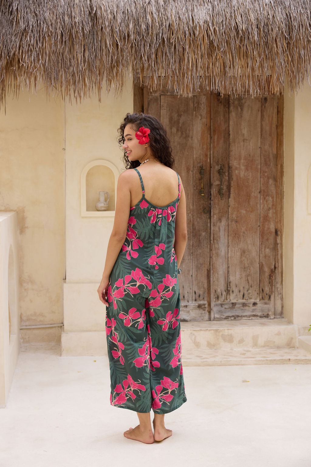 woman with brown hair wearing a dark green spaghetti strap jumpsuit with fern and ginger print