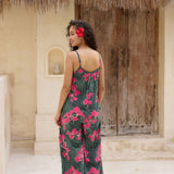 woman with brown hair wearing a dark green spaghetti strap jumpsuit with fern and ginger print