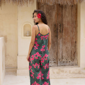 woman with brown hair wearing a dark green spaghetti strap jumpsuit with fern and ginger print