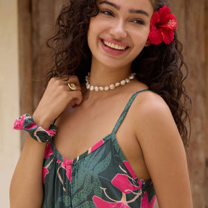 woman with brown hair wearing a dark green spaghetti strap jumpsuit with fern and ginger print