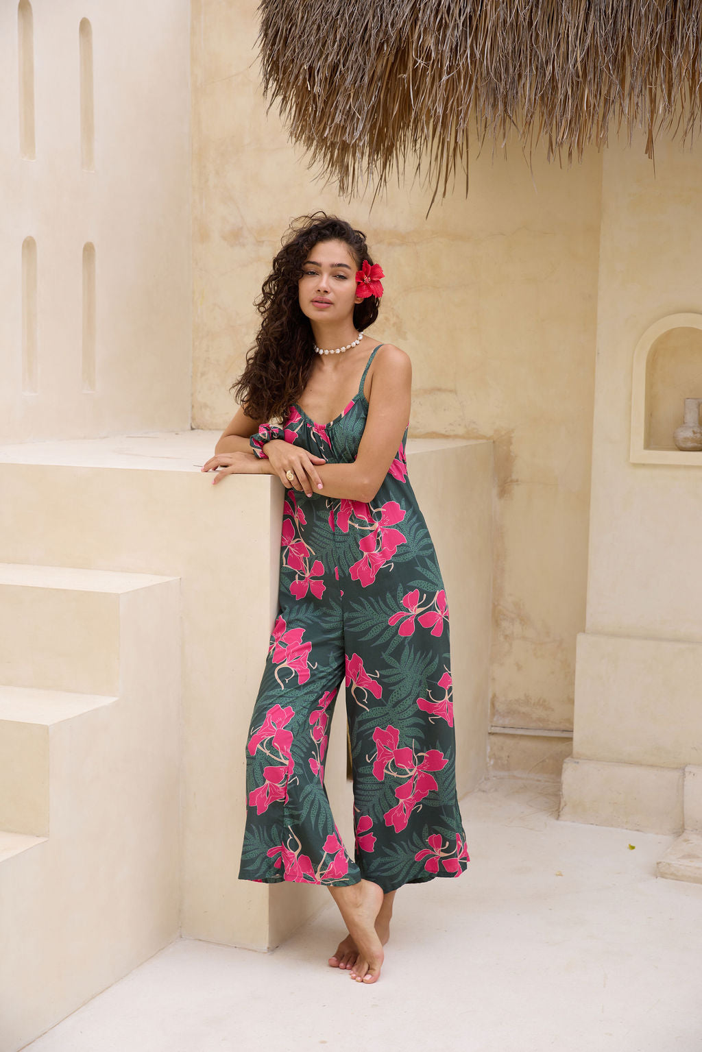 woman with brown hair wearing a dark green spaghetti strap jumpsuit with fern and ginger print