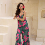 woman with brown hair wearing a dark green spaghetti strap jumpsuit with fern and ginger print