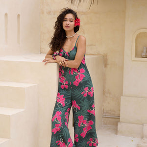 woman with brown hair wearing a dark green spaghetti strap jumpsuit with fern and ginger print