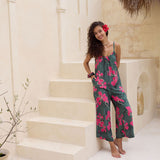 woman with brown hair wearing a dark green spaghetti strap jumpsuit with fern and ginger print