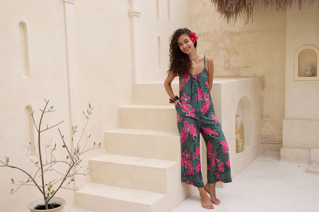 woman with brown hair wearing a dark green spaghetti strap jumpsuit with fern and ginger print