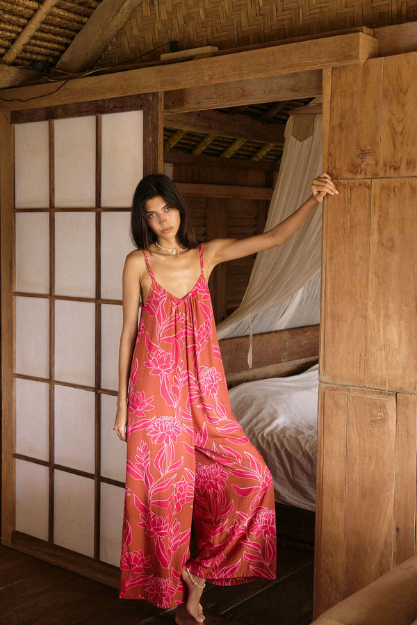 A woman with dark hair wears a YIREH v-neck, wide legged jumpsuit. It is the Laney Jumpsuit in the Garden 'Awapuhi print. 