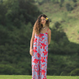 woman with brown hair wearing a jumpsuit with periwinkle background and bright red hibiscus print.