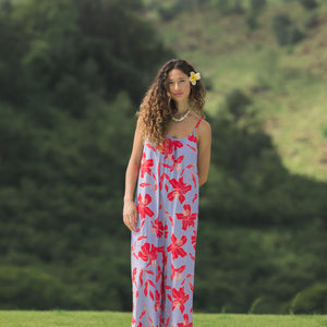 woman with brown hair wearing a jumpsuit with periwinkle background and bright red hibiscus print.