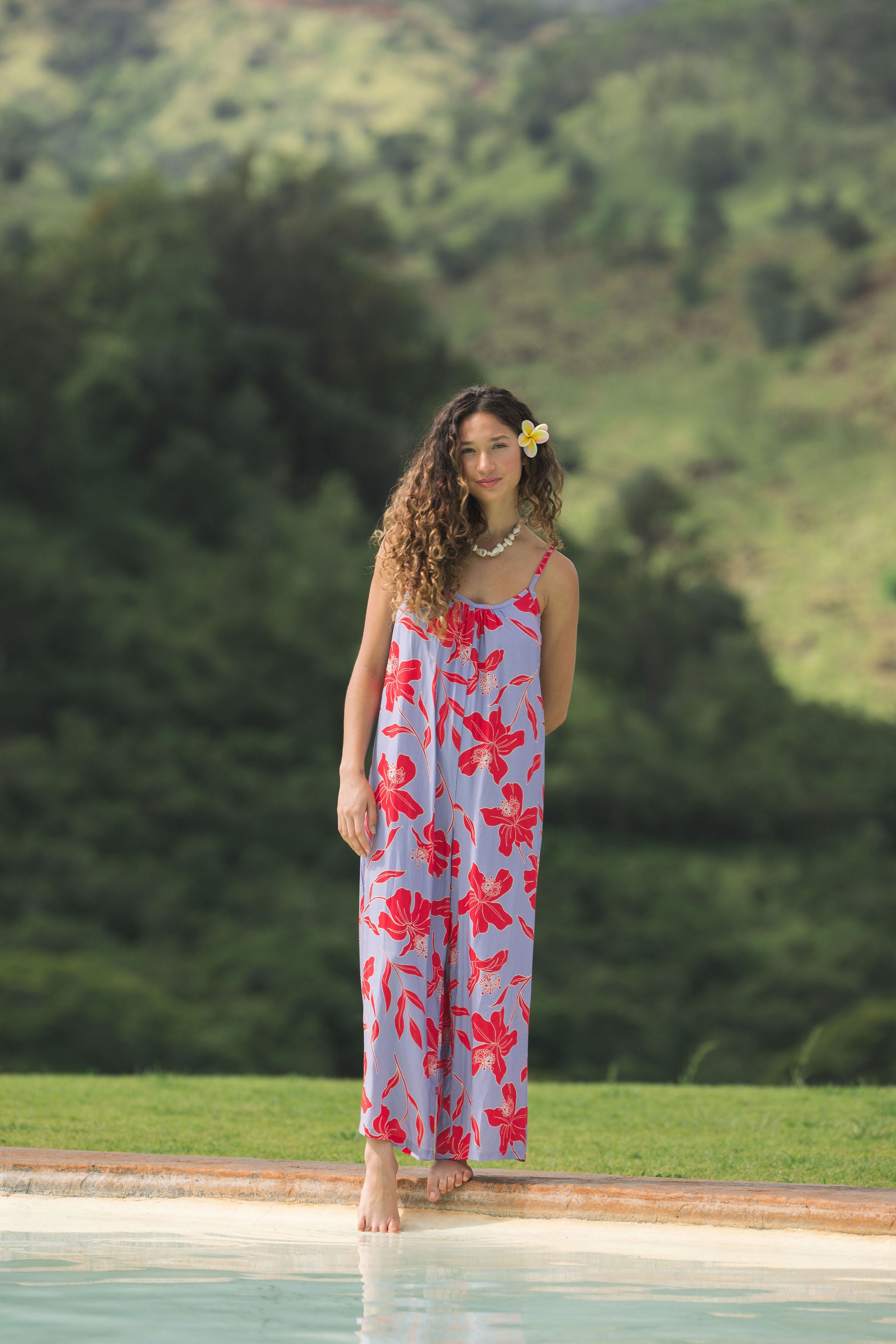 woman with brown hair wearing a jumpsuit with periwinkle background and bright red hibiscus print.
