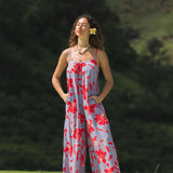 woman with brown hair wearing a jumpsuit with periwinkle background and bright red hibiscus print.