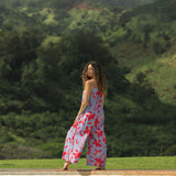 woman with brown hair wearing a jumpsuit with periwinkle background and bright red hibiscus print.