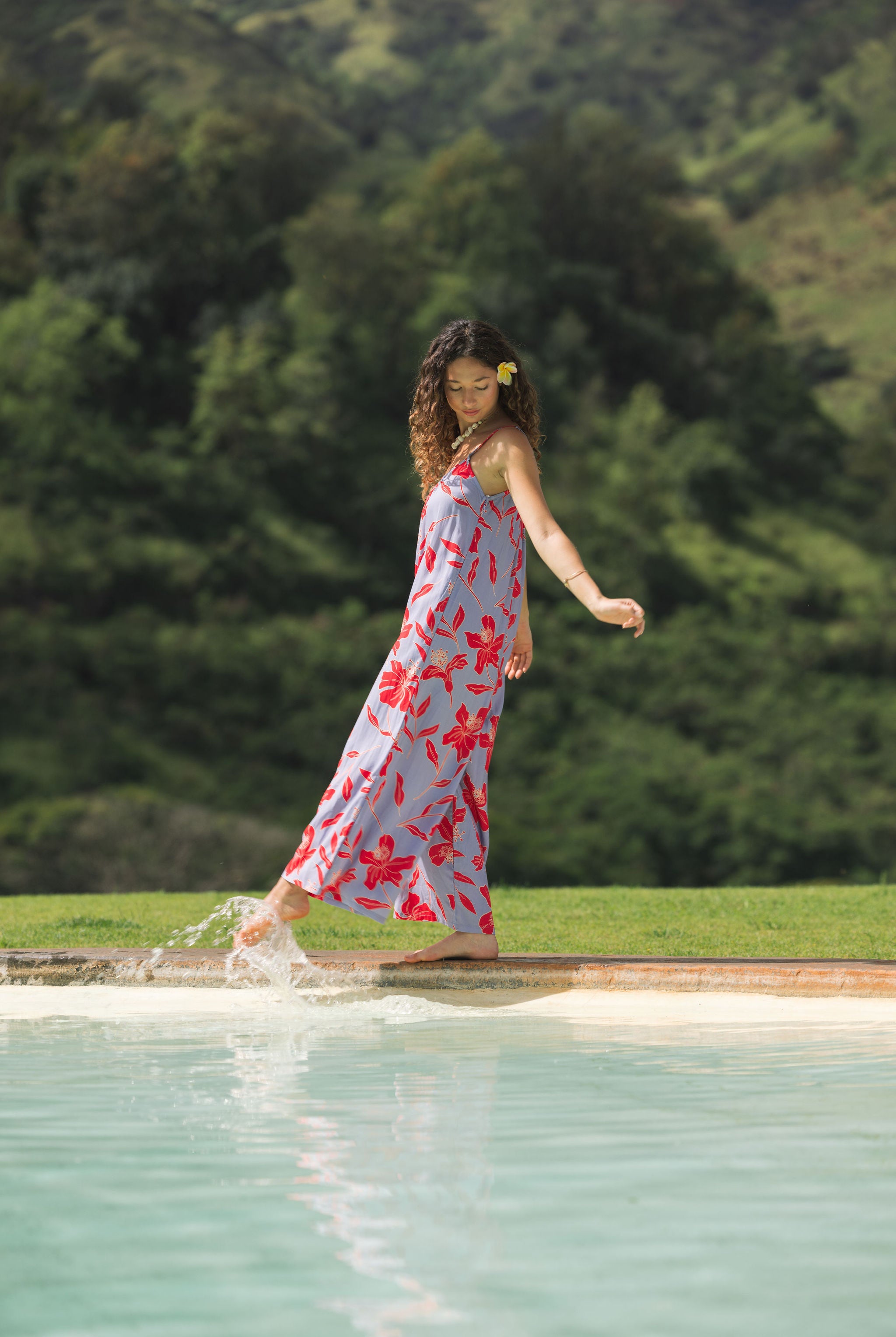 woman with brown hair wearing a jumpsuit with periwinkle background and bright red hibiscus print.